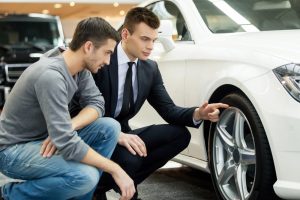 Car Loans Banner - Man examining the wheels of a new car at a dealership with a salesman