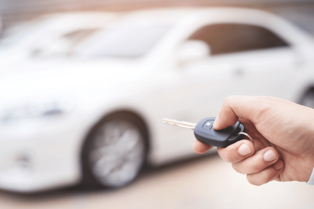 Car Loans Banner - Hand holding the keys to a new white car, pictured in the background