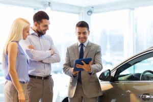 Happy couple with car salesman at dealership