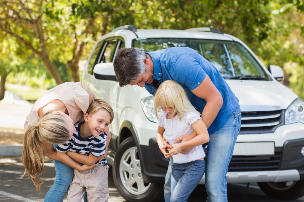 Car Loans Banner - Happy family playing outside in front of their car