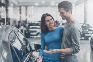 Car Loans Banner - Young couple smiling at each other after buying a car at a dealership
