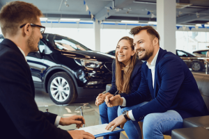 Car Loans Banner - Couple discussing a contract to buy a car at a dealership with a salesman