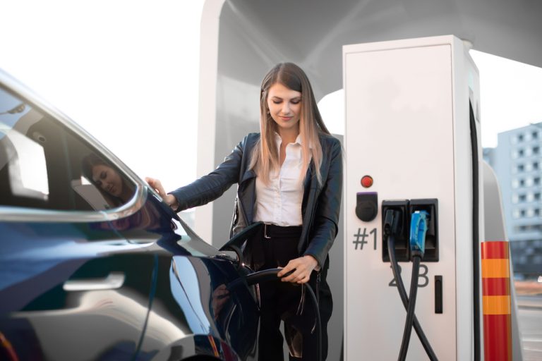 Young woman charging a dark blue electric vehicle at a charging station
