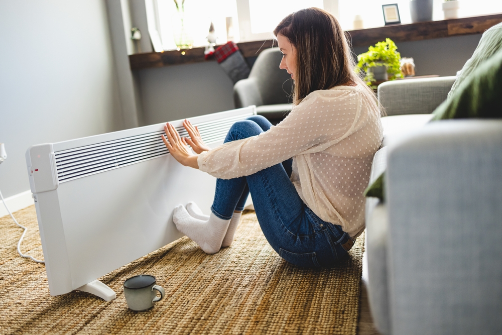 Young woman sitting in front of heater, keeping warm in winter
