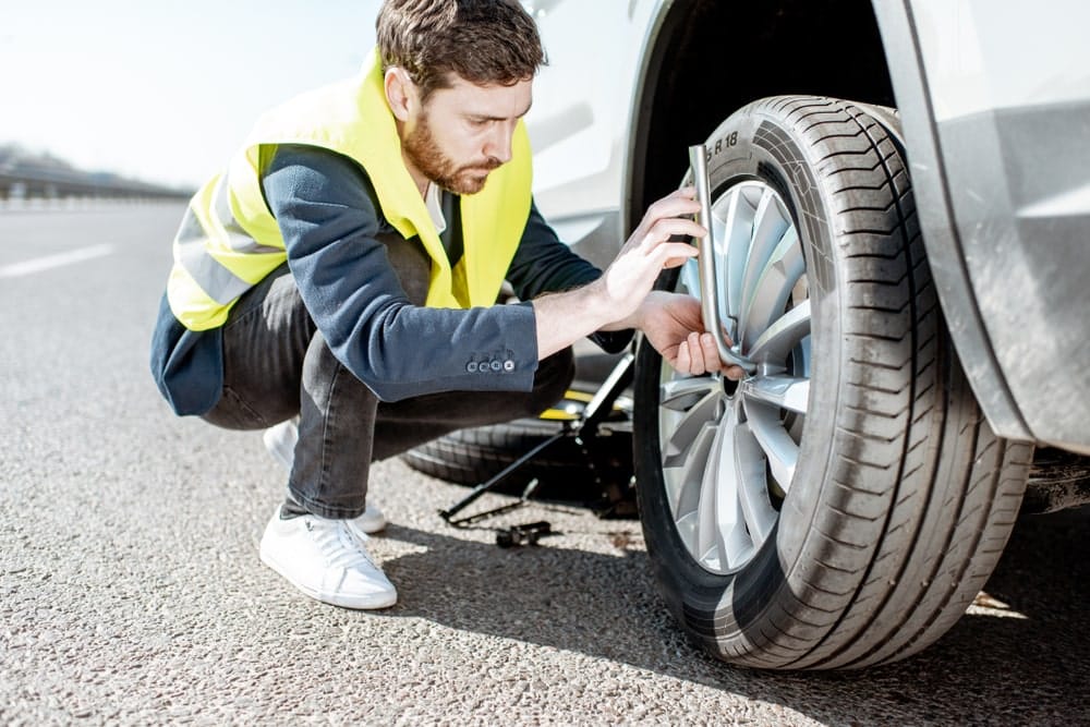 Car Insurance Banner - Roadside assistance worker repairing the wheel on a car.