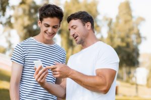 Health Insurance Banner - Father showing his dependent son something on his phone in the park