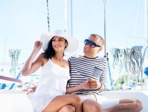 Travel Insurance Banner - Couple smiling and sitting on a boat on a sunny day.