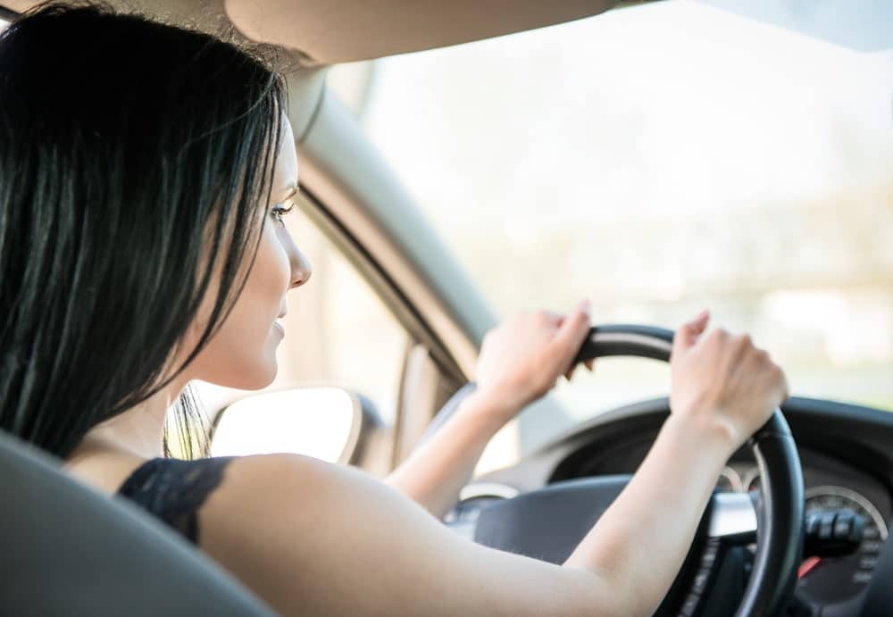 Car Insurance Banner - Rear view of young woman driving car, uncertain about driving without car insurance.