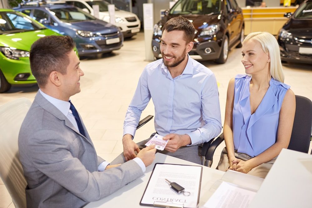 Car Insurance Banner - Couple signing their car purchase and cover note contract at a dealership.