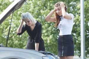 Car Insurance Banner - Two worried women examining the engine of their car after it has broken down on the road.
