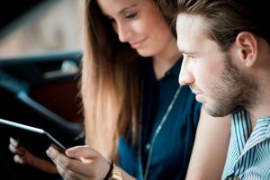 Car Insurance Banner - A young couple sitting in their car checking their car insurance policy on a tablet.