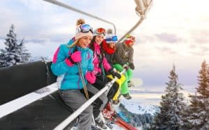 Travel Insurance Banner - Group of young friends smiling on a ski lift overlooking the snow.