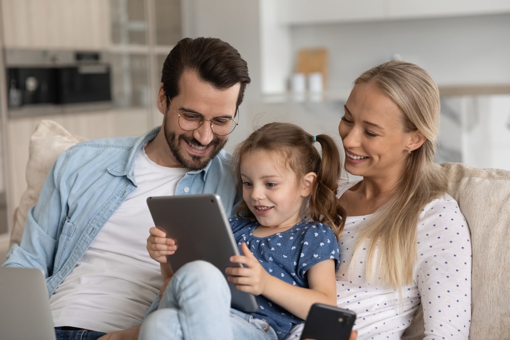 Health Insurance Banner - Young couple looking at a tablet screen with their daughter