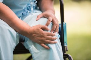 Health Insurance Banner - Elderly woman in a wheelchair in hospital garments grabbing her knee