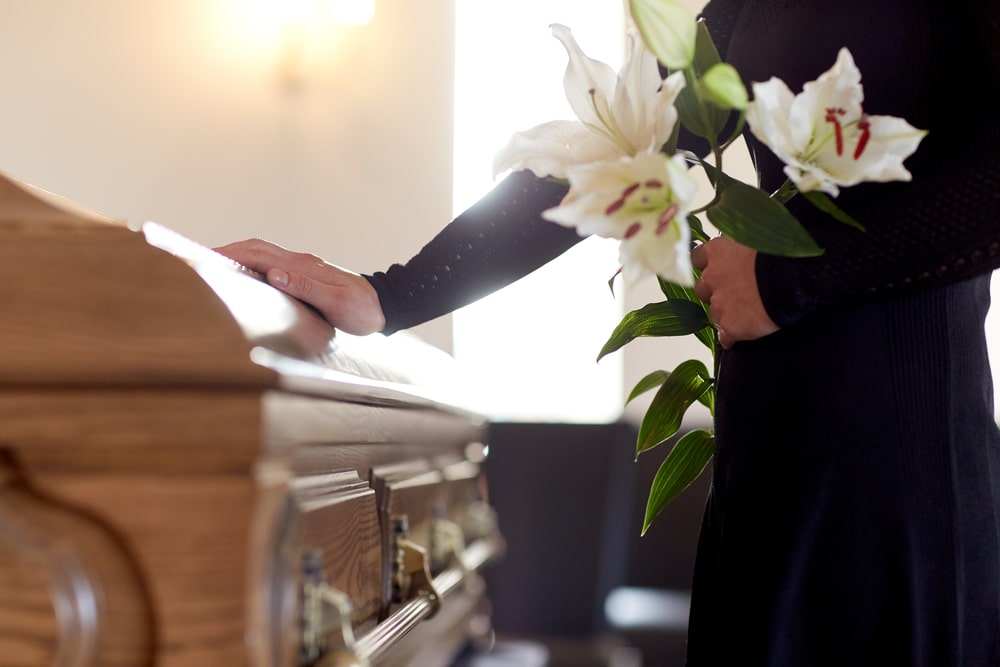 Life Insurance Banner - A woman holding flowers placing her hand on a coffin at a funeral
