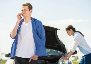 Car Insurance Banner - Man on the phone standing in front of his broken down car, which his girlfriend is looking at