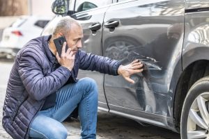 Car Insurance Banner - Man on the phone to his insurer after hit-and-run damage to his car