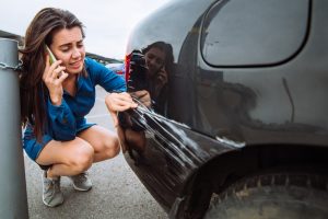 Car Insurance Banner - Young woman on the phone to her insurer after scratching the rear of her car