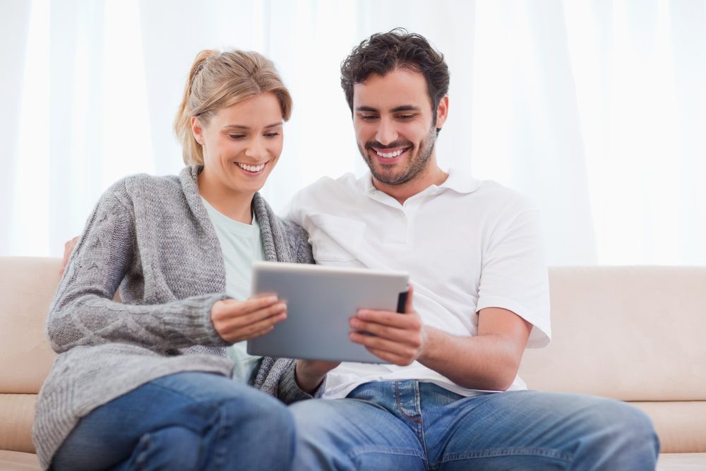 Internet Banner - Young couple sitting on the couch comparing internet plans on their tablet