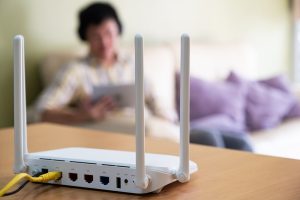 Internet Banner - Internet modem router sitting on a table while a woman uses her tablet in the background