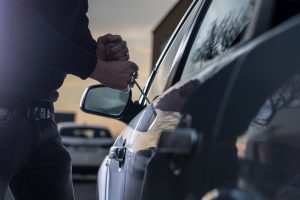Thief breaking into a car at dusk in a car park