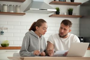 Bank Accounts Banner - Young couple discuss transferring a large sum of money while sitting in the kitchen with a laptop