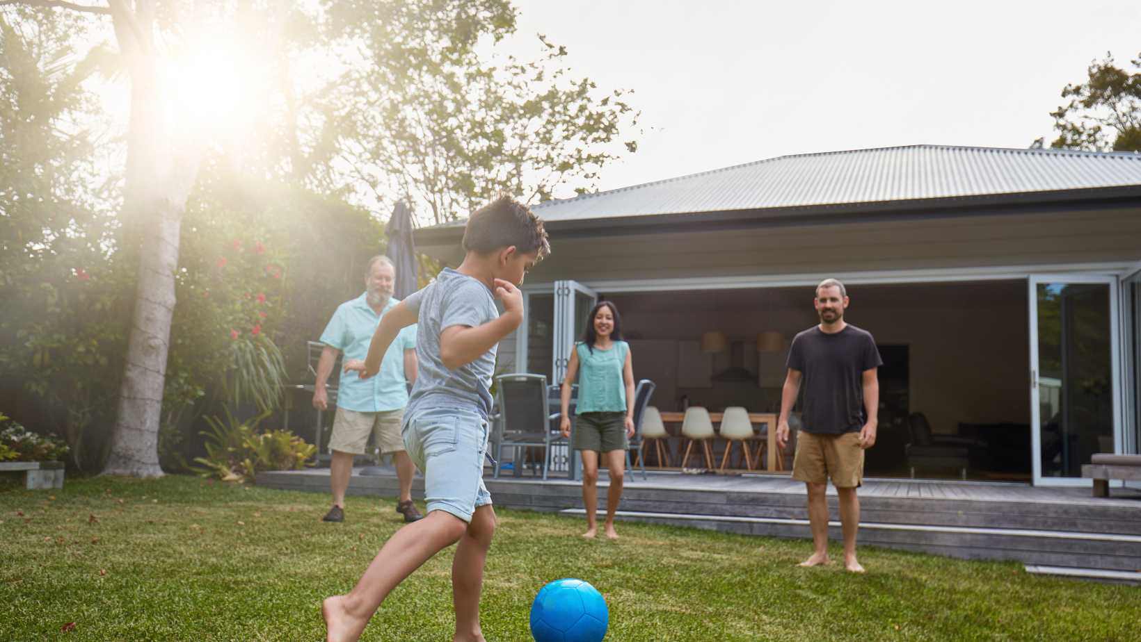 Child kicking ball in back yard with parents and grandfather
