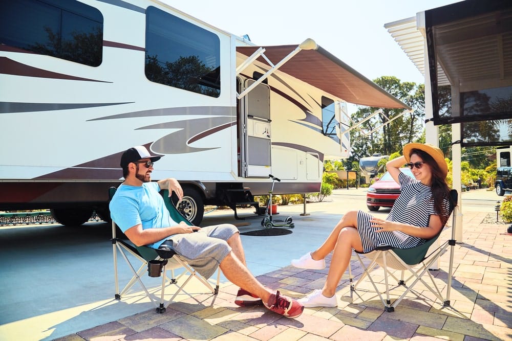 Caravan Loans Banner - Couple sitting on camper chairs outside their caravan in a caravan park