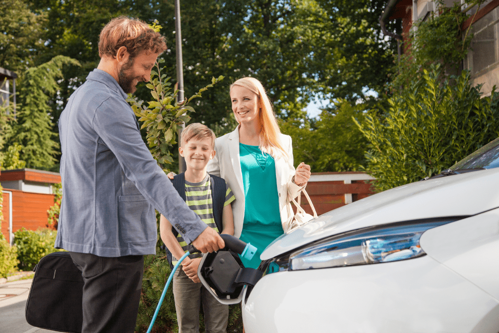 Car Loans Banner - Man charging his electric car while his wife and child stand with him